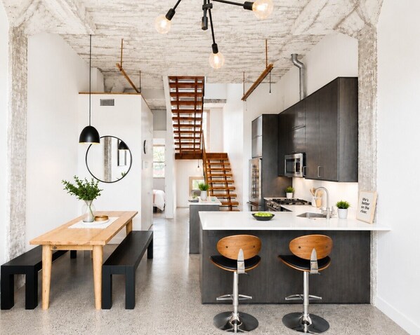 A modern kitchen with a central island, bar stools, a wooden bench, and a staircase leading to an upper level.