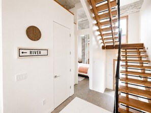 Un escalier menant à une chambre à coucher où se trouvent un lit, une porte portant l’inscription « RIVIÈRE » et une horloge murale.