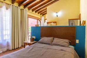A bedroom with a wooden headboard, a bedside table with a lamp, and a window with curtains. - Maito Suite - Romantic Zone (Puerto Vallarta)