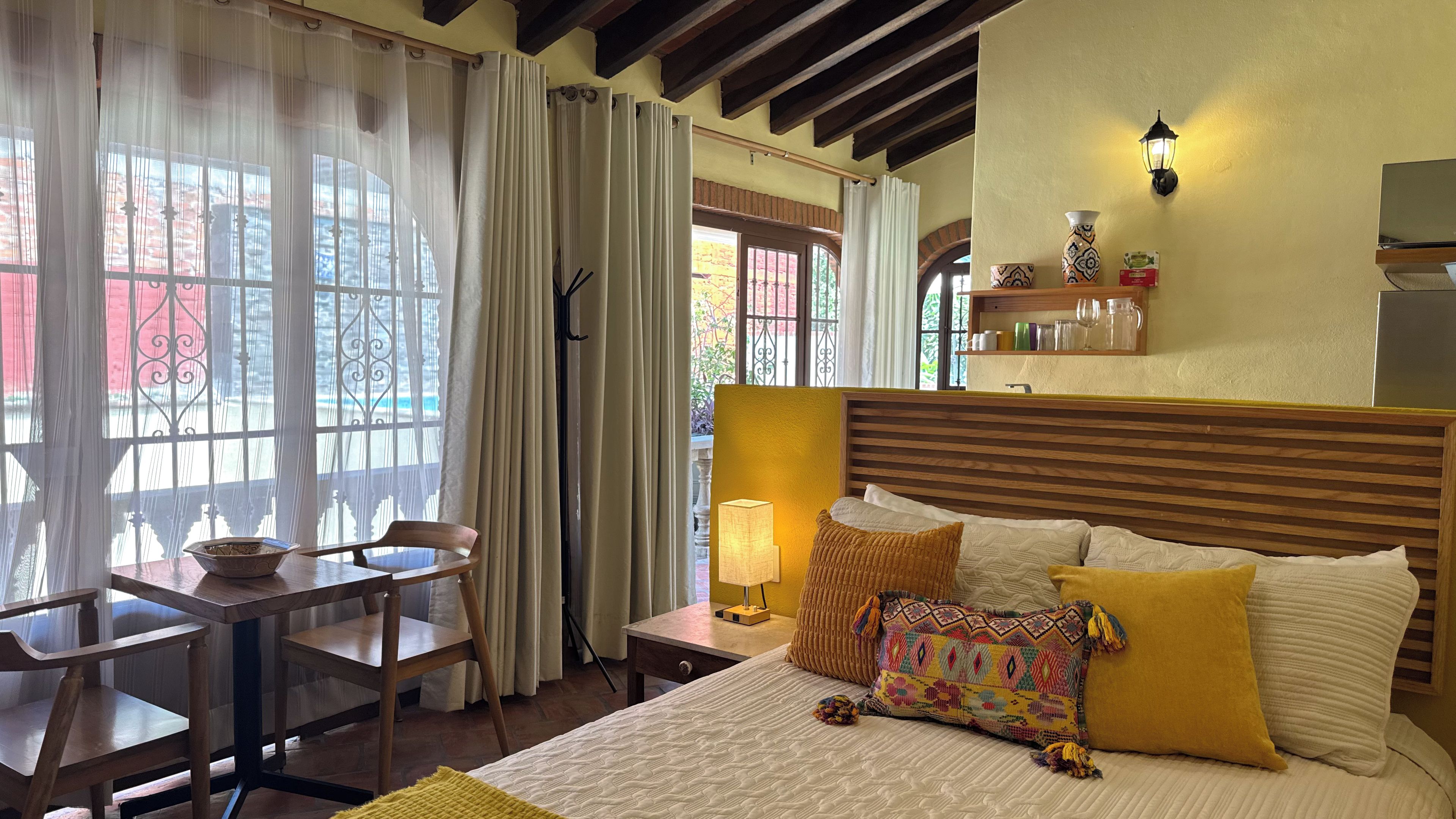 A hotel room with a bed, a table with chairs, a lamp, and a view of the outside.