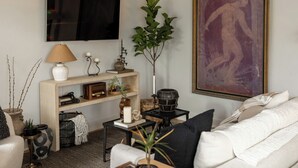 Una sala de estar con televisor, sofá, mesa de centro y un cuadro en la pared.