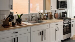Una cocina moderna con gabinetes blancos, un lavamanos de acero inoxidable, una estufa y un microondas.
