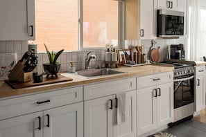 A modern kitchen with white cabinets, a stainless steel sink, a stove, and a microwave. - Modern Rooftop Retreat Near Downtown SD (San Diego)