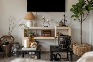 A living room with a television mounted on the wall, a wooden shelf with decorative items, a radio, and a potted plant. - Modern Rooftop Retreat Near Downtown SD (San Diego)