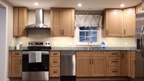 A kitchen with wooden cabinets, stainless steel appliances, and a window with a view. - The Foxboro Game Day House — 7 Min to Gillette (Foxborough)
