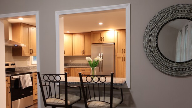 A modern kitchen with wooden cabinets, a stainless steel refrigerator, and a bar area with two chairs. - The Foxboro Game Day House — 7 Min to Gillette (Foxborough)