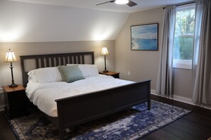 Een slaapkamer met een bed, twee nachtkastjes met lampen, een plafondventilator, een raam met gordijnen en een schilderij aan de muur.