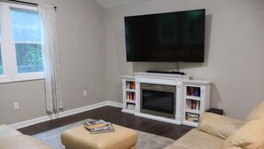 A living room with a flat-screen TV, a fireplace, a sofa, and a bookshelf. - The Foxboro Game Day House — 7 Min to Gillette (Foxborough)