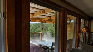 Eine Holzterrasse mit Whirlpool, Tisch und Stühlen mit Blick auf eine üppige grüne Landschaft.