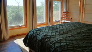 Ein Schlafzimmer mit einem großen Bett, zwei Vorhängen und einem Blick auf Bäume.