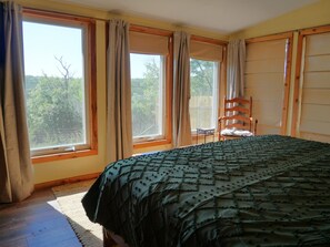 Ein Schlafzimmer mit einem großen Bett, zwei Vorhängen und einem Blick auf Bäume.