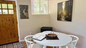 A dining area with a round table, white chairs, a wooden sideboard, and two paintings on the walls. - The Lookout at Silver Springs! Mountain air and Trout Pond Fun-sleeps up to 5 (Cloudcroft)