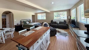 A spacious room with a wooden dining table, a bed with a green bedspread, a gray sofa, and a television. - The Lookout at Silver Springs! Mountain air and Trout Pond Fun-sleeps up to 5 (Cloudcroft)