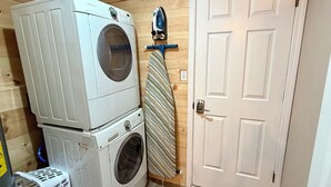 A laundry area with stacked washers and dryers, an ironing board, and a door. - The Lookout at Silver Springs! Mountain air and Trout Pond Fun-sleeps up to 5 (Cloudcroft)