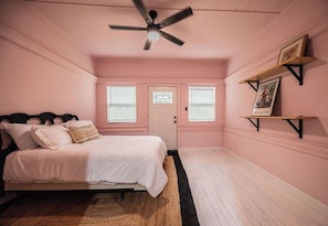 Un dormitorio con una cama, ventilador de techo, puerta y ventana con persianas.