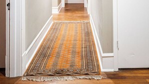 Un couloir avec un tapis à motifs, des murs blancs et des œuvres d’art encadrées.