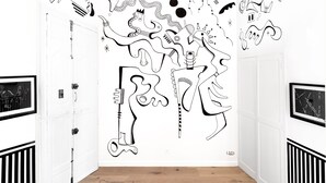 A hallway with a white wall featuring abstract black line art. There are two doors on either side, each with a black and white framed picture above them. The floor is wooden. - L'Atelier des Merveilles - Sur le port de Sète (Sète)