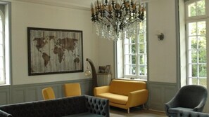 A room with a large world map on the wall, a chandelier, a yellow sofa, and a grey armchair. - Château de la Bouleaunière - Avec 3 ha de jardin (Grez-sur-Loing)