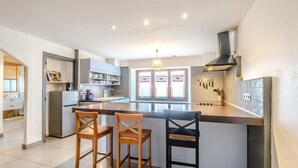 Eine moderne Küche mit einer zentralen Kochinsel, zwei hölzernen Barhocker, einem eingebauten Backofen und einem Fenster mit herzförmigen Verzierungen.