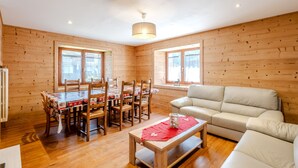 Ein Zimmer mit Holzwänden, einem Esstisch, Stühlen, einer Couch und einer roten Tischläufer.