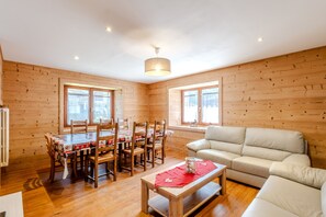 A wooden-paneled room with a dining table, chairs, a sofa, and a red table runner. - Le Col de Feu - Joli duplex pour 8 avec jardin (Lullin)