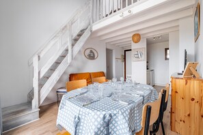 A dining area with a round table set for four, a staircase, and a wooden cabinet. - Les 4 Voiles - À 280 m de la plage (Damgan)
