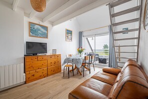 A modern living room with a TV, wooden dresser, dining table, and leather sofa. - Les 4 Voiles - À 280 m de la plage (Damgan)