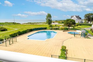 A swimming pool area with a view of the sea, a house in the background, and a paved walkway. - Les 4 Voiles - À 280 m de la plage (Damgan)