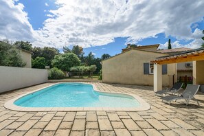 Ein Pool mit gefliestem Sonnendeck, Liegestühlen und einem Gebäude mit einem Ziegeldach.