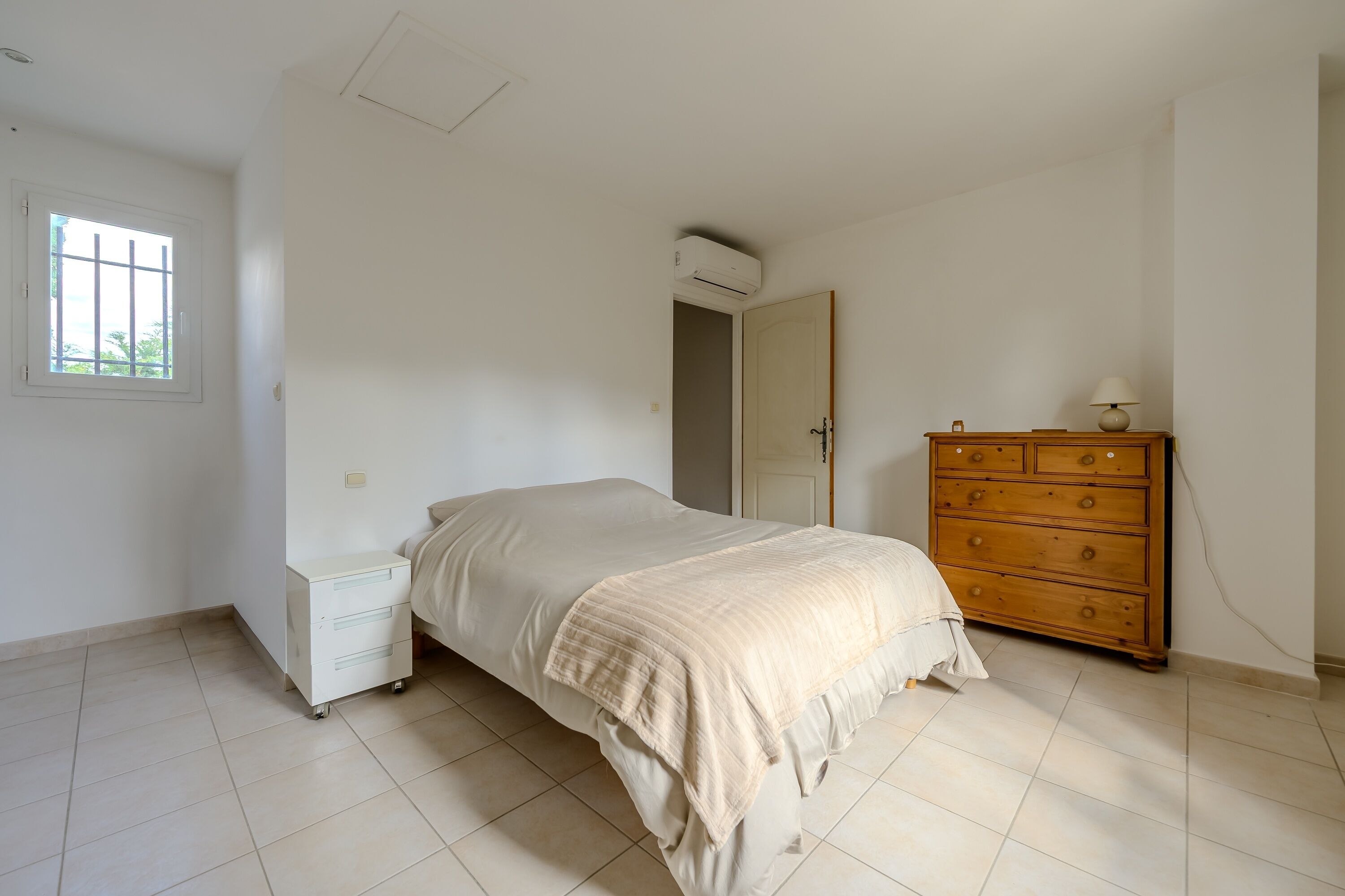 Une chambre à coucher comprenant un lit, une commode, une fenêtre et un appareil de climatisation.