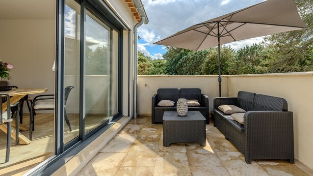 A patio with a glass door, outdoor furniture, and a large umbrella. - Les Oliviers du Papet - Le Nid (Châteaurenard)
