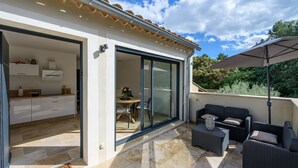 A modern patio with outdoor furniture, a sliding glass door leading to a kitchen, and a clear sky. - Les Oliviers du Papet - Le Nid (Châteaurenard)