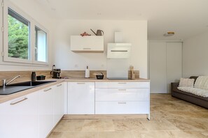 A modern kitchen with white cabinets, a built-in oven, and a window. - Les Oliviers du Papet - Le Nid (Châteaurenard)