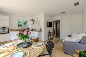 A modern kitchen with a dining area, a grey sofa, and a TV mounted on the wall. - Les Oliviers du Papet - Le Nid (Châteaurenard)