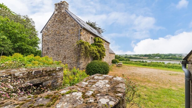 Une maison en pierre recouverte de lierre, une pelouse et une rivière en arrière-plan.