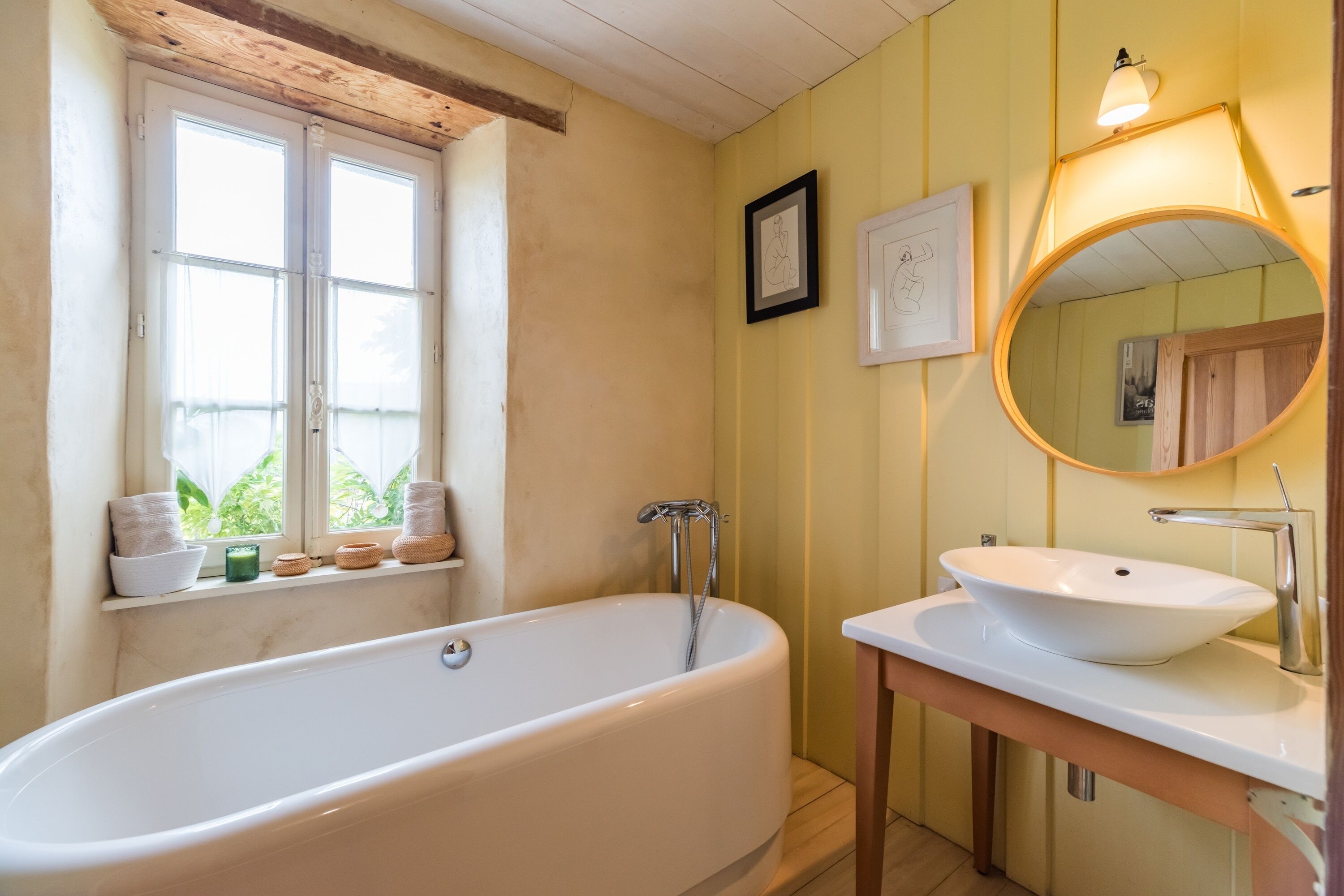 A bathroom with a bathtub, a sink, a mirror, and a window with towels.