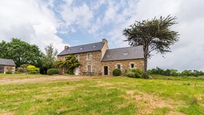 Une maison en pierre avec une cour verdoyante, un grand arbre et un ciel dégagé.
