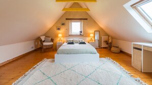 Une chambre avec un plafond en pente, un lit, deux lampes de chevet, une fenêtre, une chaise et une table de chevet.