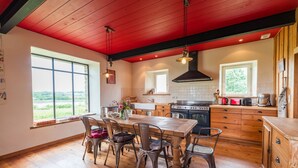 Une cuisine avec une table et des chaises en bois, un poêle et une fenêtre donnant sur un paysage verdoyant.