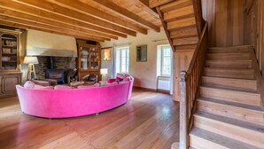 Un intérieur en bois avec un canapé rose aux lignes courbes, une cheminée, des étagères et un escalier en bois.