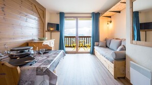 A room with a dining table set, a sofa, a TV, and a balcony with a view. - Les Alpages du Corbier B108 - Télésièges à 250 m (Villarembert)