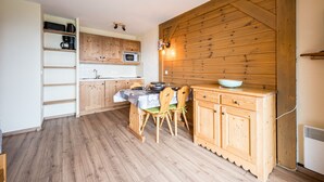 A kitchen with wooden cabinets, a dining table with chairs, and a microwave. - Les Alpages du Corbier B108 - Télésièges à 250 m (Villarembert)