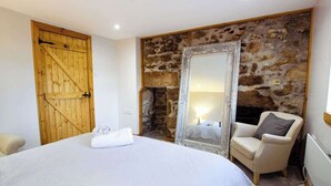A bedroom with a large bed, a stone wall, a wooden door, and a mirror. - 5 Bed, 2 Bath Cottage with HotTub & Sauna (Aberdeenshire)