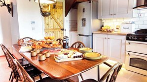 A wooden dining table with a variety of food items and plates, a refrigerator, oven, and a kitchen counter with a bread sign. - 5 Bed, 2 Bath Cottage with HotTub & Sauna (Aberdeenshire)