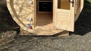 A wooden, dome-shaped structure with an open door revealing a fireplace and a small table. - 5 Bed, 2 Bath Cottage with HotTub & Sauna (Aberdeenshire)