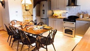 A kitchen with a dining table, chairs, a refrigerator, oven, and a hanging light fixture. - 5 Bed, 2 Bath Cottage with HotTub & Sauna (Aberdeenshire)