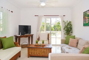 Ein Wohnzimmer mit Sofa, Couchtisch, Fernseher und Blick ins Freie.