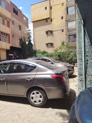 A parking area with multiple cars, buildings with balconies, and a clear sky. - Apartment in very quiet area 5 mn from piramides, (Guiza)