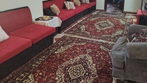 Ein Wohnzimmer mit einem roten Sofa, einem grauen Sessel, einem gemusterten Teppich und einem Deckenventilator.