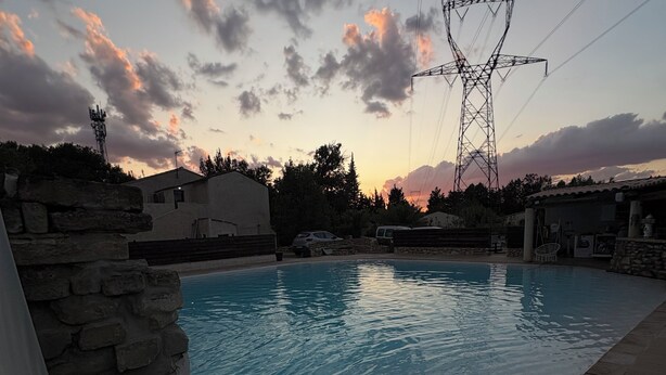 A swimming pool with a stone border, a stone wall, and a power line structure in the background. - Loft "The Jungle (Châteaurenard)